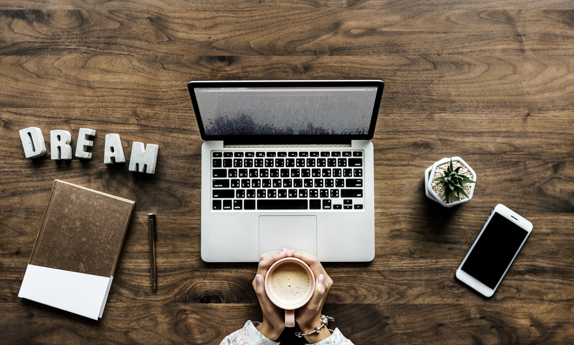 laptop on desk and person holding coffee